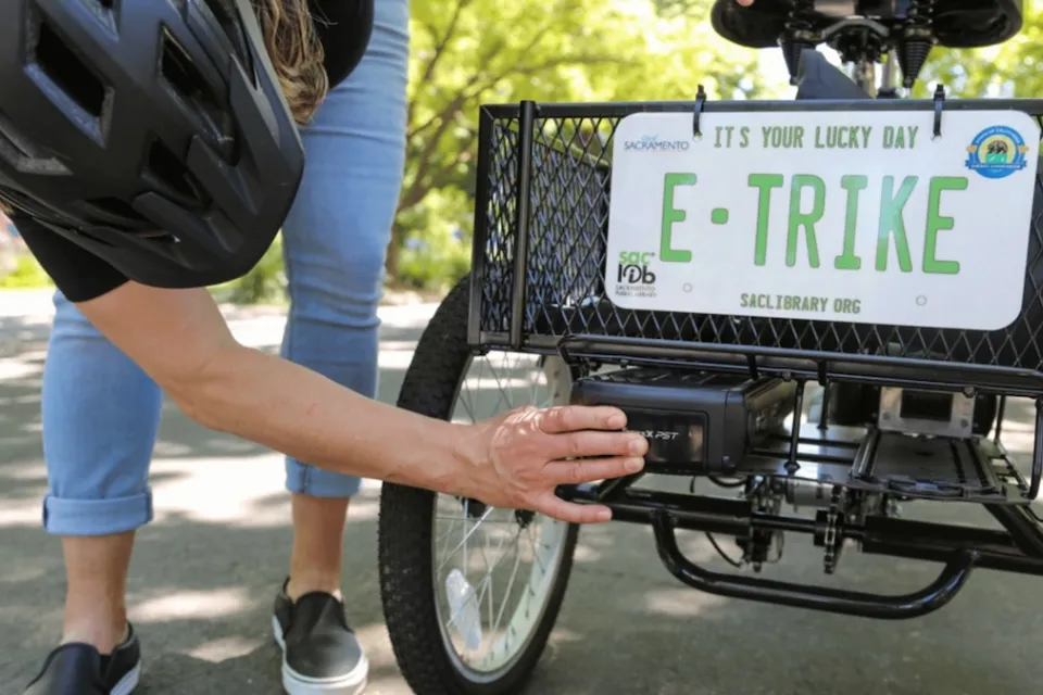 Close-up of person putting sticker on back of basket of electric tricycle with mock license plate reading "E-TRIKE."